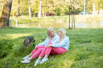 Family relations. Happy mom and daughter are dressed same and enjoy socializing sitting in park on grass. Love. 