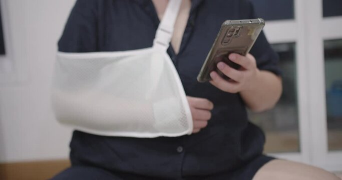 closeup young woman using holding smartphone with hand injury wear splint for fast recovery. Injured female with cast or sling on shoulder, life insurance accident and healthcare concept