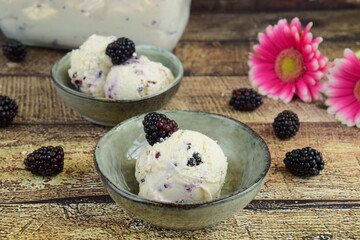ice cream in a bowl ,ripe blackberries on the table. summer treats. wooden background. Decorated with pink flower. Selective focus