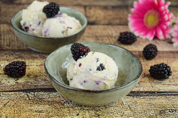 ice cream in a bowl ,ripe blackberries on the table. summer treats. wooden background. Decorated with pink flower. Selective focus