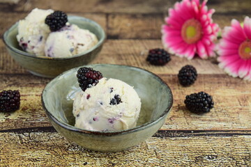 ice cream in a bowl ,ripe blackberries on the table. summer treats. wooden background. Decorated with pink flower. Selective focus