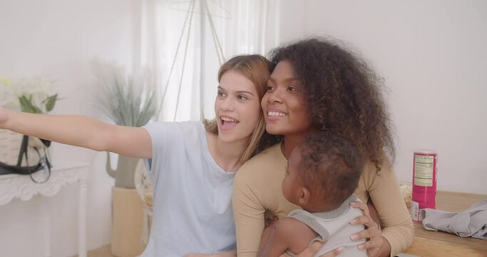 Happy young homosexual female gay lesbian couple with son toddler baby boy is making taking selfie together or video call to friends or relatives in a living room at home, Concept of LGBTQ+
