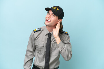 Young safeguard man isolated on blue background listening to something by putting hand on the ear
