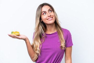 Young pretty Uruguayan woman holding a tartlet isolated on white background looking up while smiling