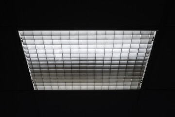 Fluorescent lamps in square lampshade with cellular mesh grid in dark room.