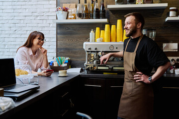 Young male barista talking to woman customer in coffee shop
