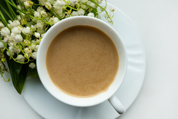 Coffee mug with a bouquet of flowers lily of the valley. View from above, the concept of morning.