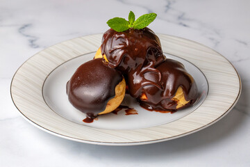 Delicious profiteroles with chocolate and white plate.