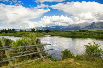A distant mountain is viewed beyond a fence and river on a sunny Summer day near Townsend, MT, USA.
