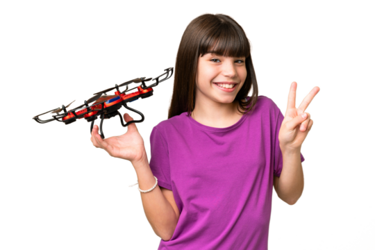 Little caucasian girl holding a drone over isolated background smiling and showing victory sign
