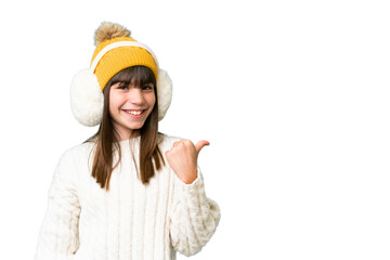 Little caucasian girl wearing winter muffs over isolated background pointing to the side to present...