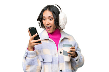 Young Argentinian woman wearing winter muffs over isolated background holding coffee to take away...