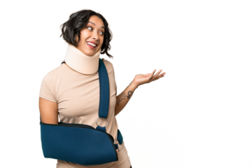 Young argentinian woman wearing neck brace and sling over isolated background with surprise expression while looking side