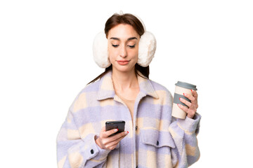 Young caucasian woman wearing winter muffs over isolated chroma key background holding coffee to...
