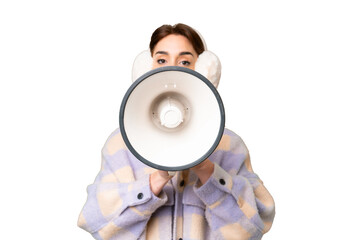 Young caucasian woman wearing winter muffs over isolated chroma key background shouting through a...