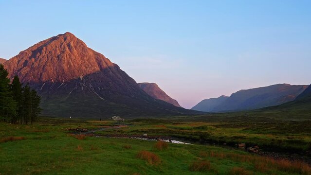 Moving through meadow towards the iconic Buachaille Etive Mor mountain covered in beautiful golden morning sunrise light on an early summer morning, Scottish Highlands, UK
