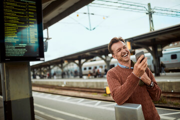 Mature man using a smart phone while waiting for his train at the train station