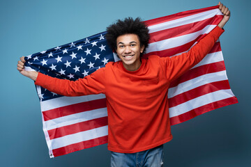 Young happy African American man holding American flag isolated on blue background