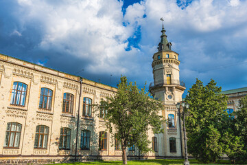 Facade of an old brick building with a tower. Building against the sky. Beautiful old architecture. University park. Tourist place. Gothic architecture.