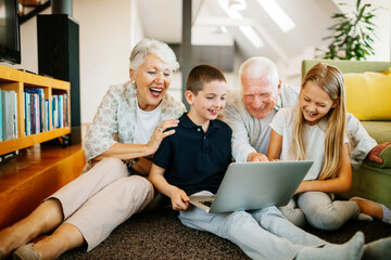 Grandparents using a laptop with their grandchildren in the living room of their home