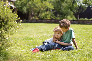 Naklejka na ściany i meble Two little brother boys lie on the grass and hug. Family ties and friendship concept