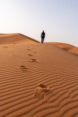 Fototapeta na wymiar A person walking through the Erg Chebbi desert in the African Sahara