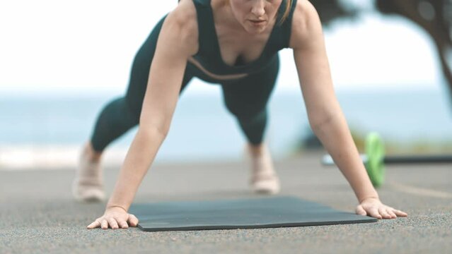 Adult athletic woman does push ups at the outdoors sports ground
