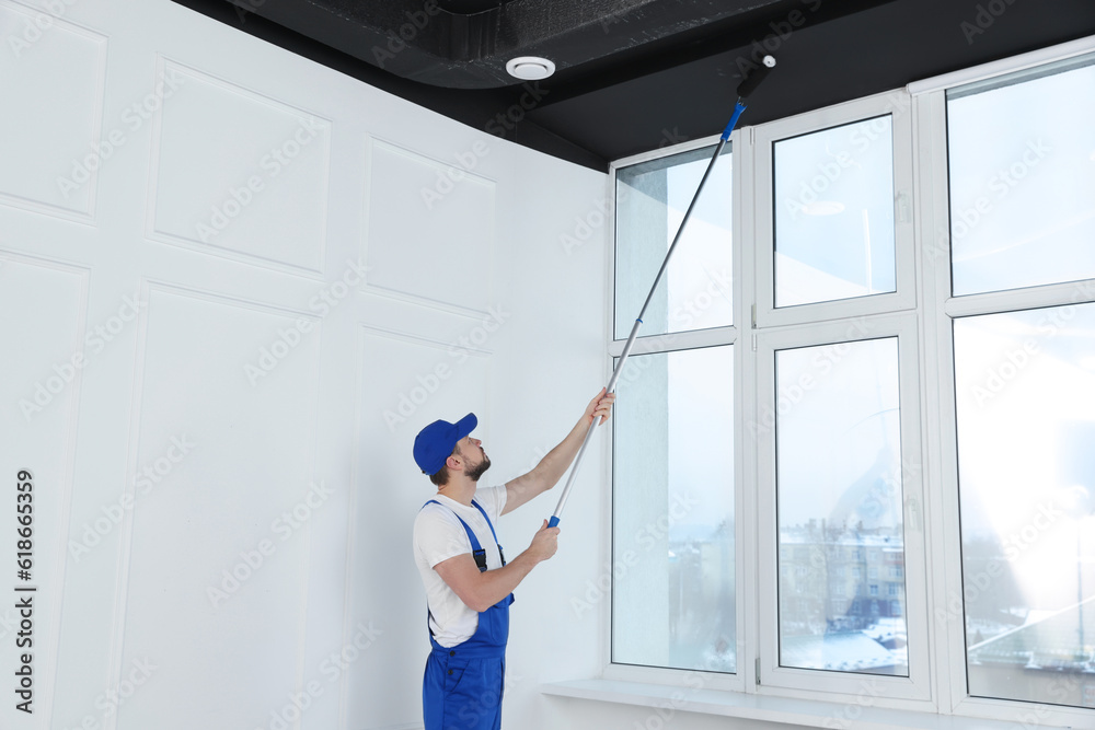 Poster Worker in uniform painting ceiling with roller indoors