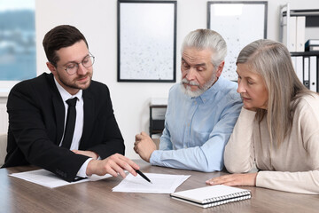 Insurance agent consulting elderly couple about pension plan at wooden table in office