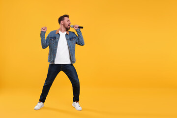 Handsome man with microphone singing on yellow background. Space for text © New Africa