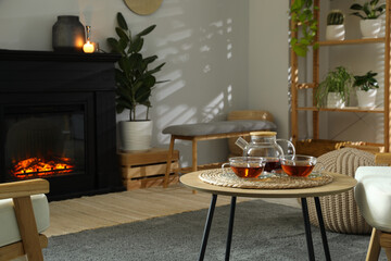 Stylish fireplace near coffee table with tea in cosy living room. Interior design