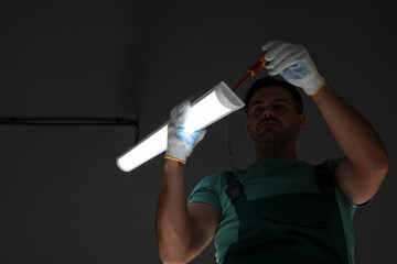 Ceiling light. Electrician installing led linear lamp indoors, low angle view. Space for text