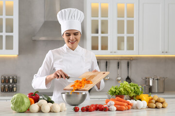 Professional chef putting cut bell pepper into metal bowl at white marble table in kitchen