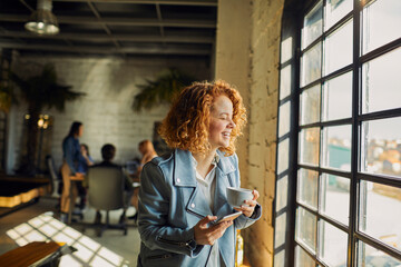 Young woman using a smart phone while looking through the window in a startup company office