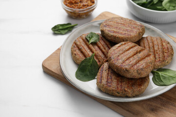 Tasty grilled vegan cutlets and spinach on white table