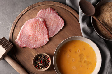 Cooking schnitzel. Raw pork slices, other ingredients and meat tenderizer on grey textured table, flat lay