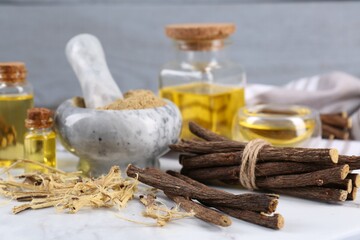 Dried sticks of licorice roots, powder and essential oil on white table, closeup