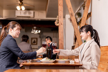 ワインバー・レストラン・バルで女子会をするスーツ姿の笑顔のアジア人女性
