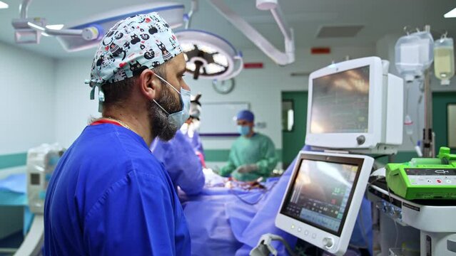 Bearded anesthesiologist watching intently the monitors of equipment. Doctor looks at the screen of lung ventilator.