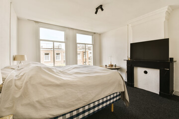 a bedroom with a bed, tv and fireplace in the corner of the room on the left is an open window