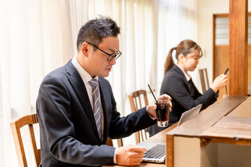カフェのカウンターでノートパソコンを使う眼鏡のアジア人のビジネスマン
