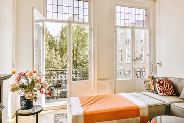 a living room with an orange blanket on the couch and two windows that look out onto the cityscapea
