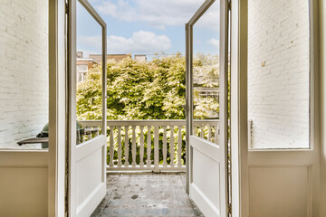 an open door leading to a balcony with white brick walls and green trees in the distance, on a sunny day