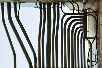 Parallel water pipes connected to concrete turn at 90 degree angles against a pale sky