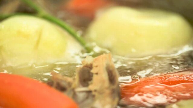 レストラン厨房の調理　大きな鍋で煮られてグツグツ煮立つたまねぎ、ニンジン、ハーブなどの野菜、鶏がらでとるフォン、出汁、スープ