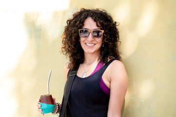 Mixed race woman smiling while drinking mate outdoors.