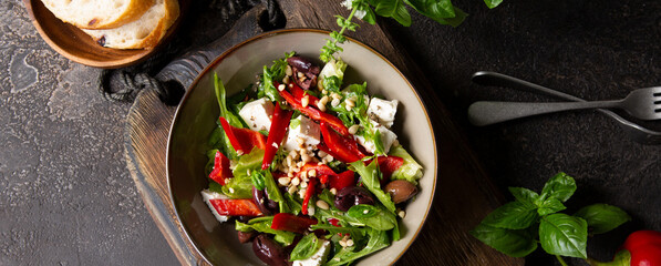 bowl with salad with arugula, bell peppers, feta cheese and olives on a dark table