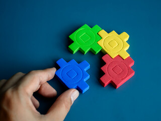 Blue jigsaw piece in hand wait to fulfill to complete with the group, red, yellow and green puzzle blocks on blue background, minimal style. Business partnership, teamwork, and solution concepts.