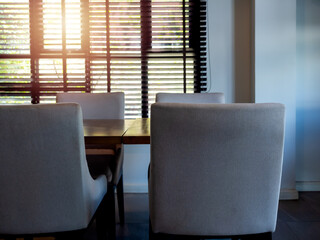 Empty modern grey fabric chairs, seat and wooden table, dining table set vintage style, near the window decorated with black louver with warm sunlight. Dining room interior design in hotel, indoor.