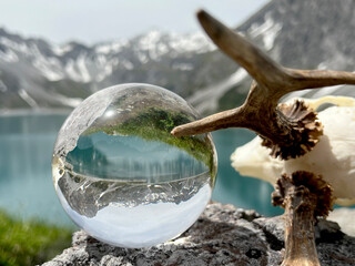 Roebuck antlers next to Lensball, crystal ball, with reflections of Lake Lunersee (Lünersee, Montafon, Vorarlberg). In the background the famous high mountains of austria and switzerland (Rätikon). - obrazy, fototapety, plakaty